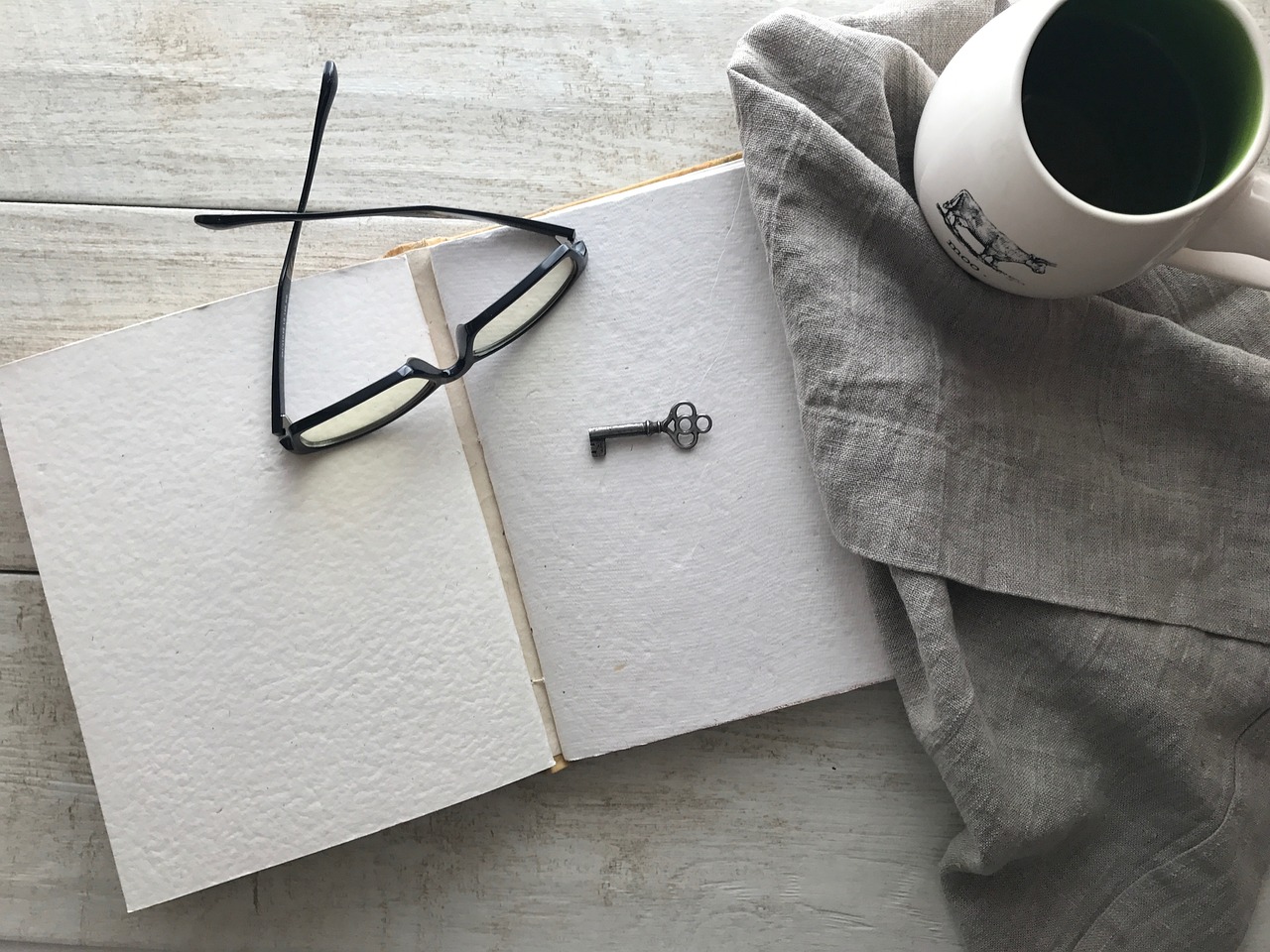 A decisão de se tornar um autor - um caderno aberto mostrando páginas em branco, um óculos sobre as páginas, xicara de café ao lado, imagem de Deborah Hudson, via pixabay.com